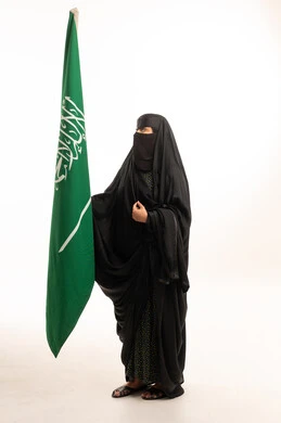 امرأة سعودية بالعباءة والنقاب مع علم السعودية
