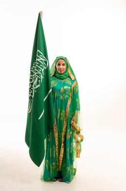 امرأة سعودية تحمل العلم بالزي التقليدي الأخضر