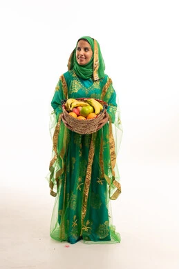 امرأة سعودية بالزي التقليدي الأخضر تحمل سلة فواكه