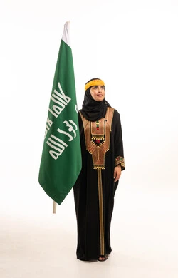 امرأة سعودية بالعباءة التقليدية مع العلم الوطني