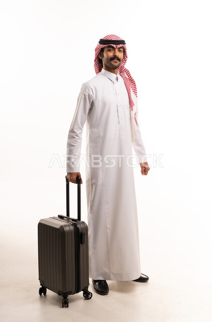 رجل سعودي يقف بجانب حقيبة سفر أمام خلفية بيضاء