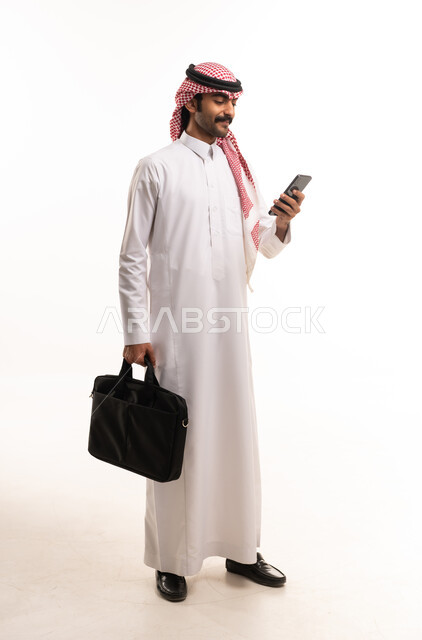 رجل أعمال سعودي يحمل هاتف ذكي وحقيبة عمل