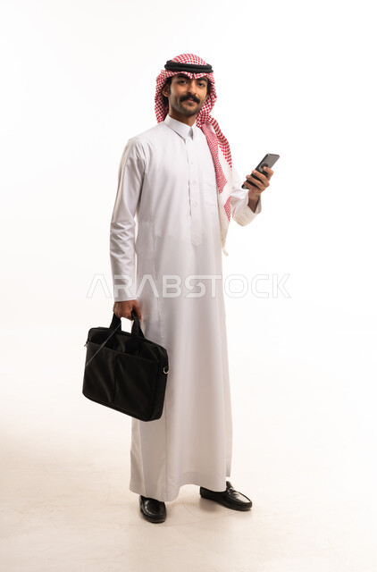 رجل أعمال سعودي يحمل هاتف ذكي وحقيبة لابتوب