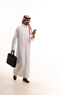 رجل أعمال سعودي يمشي مع هاتف ذكي وحقيبة عمل
