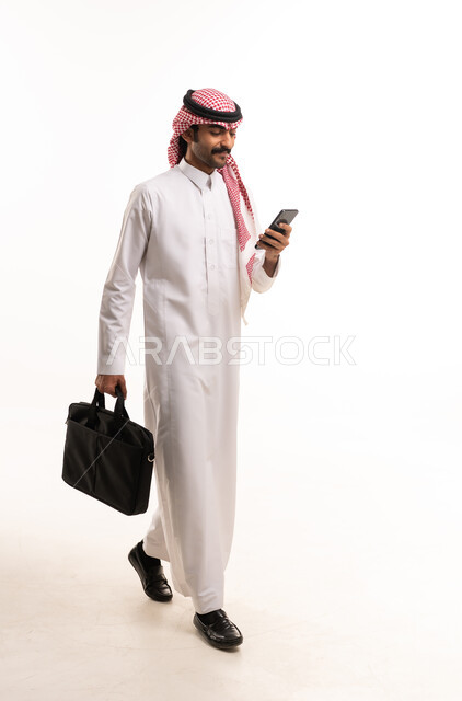 رجل أعمال سعودي يسير مع هاتف وحقيبة عمل