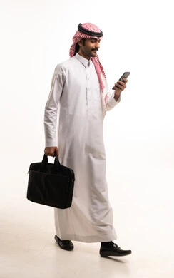 رجل أعمال سعودي يمشي مع هاتف ذكي وحقيبة عمل