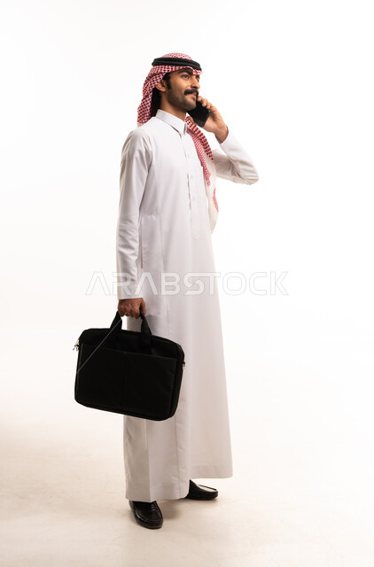 رجل أعمال سعودي بالثوب التقليدي يتحدث بالهاتف الذكي