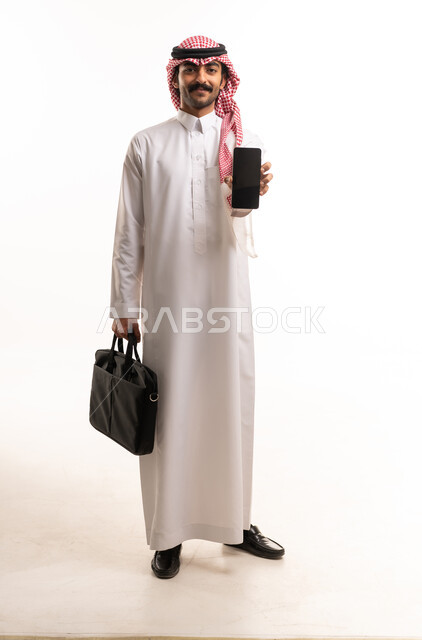 رجل أعمال سعودي يحمل هاتف ذكي وحقيبة عمل