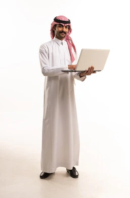 رجل سعودي بالزي التقليدي يحمل جهاز كمبيوتر محمول أبيض