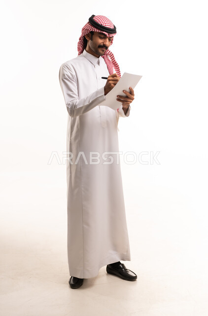 رجل سعودي بالزي التقليدي يكتب على ورقة