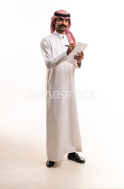 رجل أعمال سعودي بالزي التقليدي يكتب على ورقة في استوديو