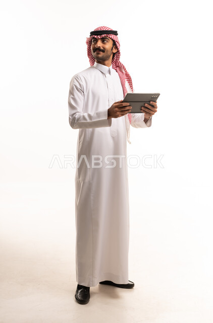 رجل سعودي يرتدي الزي التقليدي ويحمل جهاز لوحي رقمي