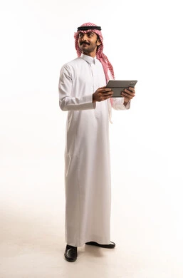 رجل سعودي يرتدي الزي التقليدي ويحمل جهاز لوحي رقمي