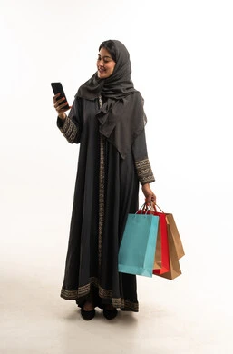 امرأة سعودية تحمل أكياس تسوق وتستخدم الهاتف