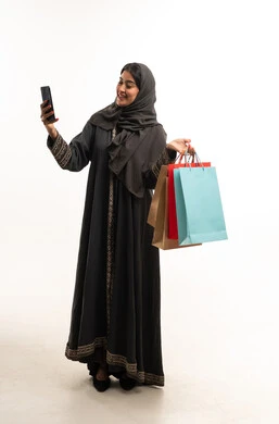 امرأة سعودية بالعباءة تحمل أكياس تسوق وهاتف