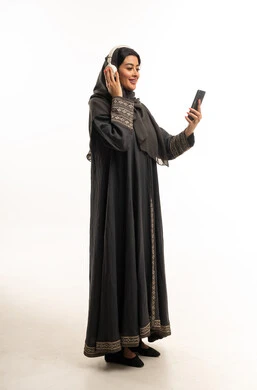 امرأة سعودية بالعباءة تستخدم الهاتف والسماعات