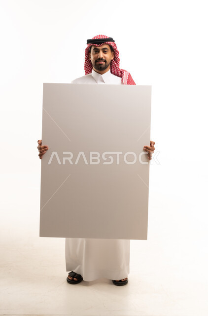 رجل سعودي بالزي التقليدي يمسك لوحة بيضاء فارغة