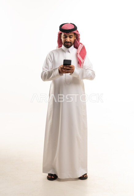 رجل سعودي بالثوب التقليدي يستخدم الهاتف الذكي بخلفية بيضاء