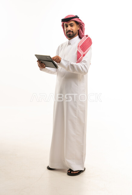 رجل سعودي بالزي التقليدي يستخدم جهازاً لوحياً