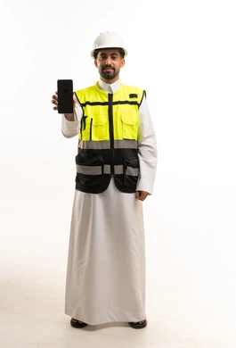 مهندس سعودي يرتدي سترة السلامة ويحمل هاتفاً ذكياً
