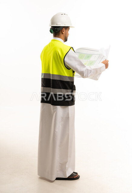 مهندس سعودي يرتدي سترة السلامة ويمسك مخططات بناء
