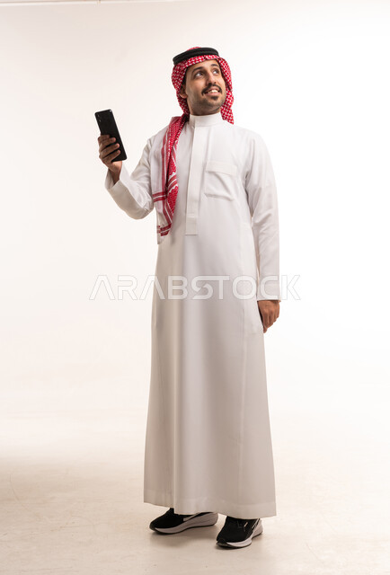 رجل سعودي بالزي التقليدي يحمل هاتفاً ذكياً في استوديو