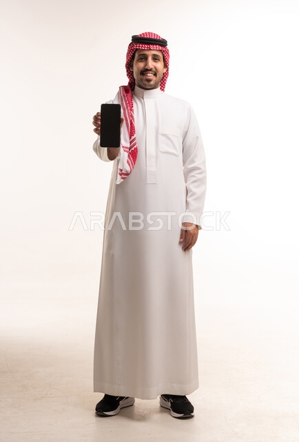 رجل سعودي بالزي التقليدي يحمل هاتف ذكي في الاستوديو