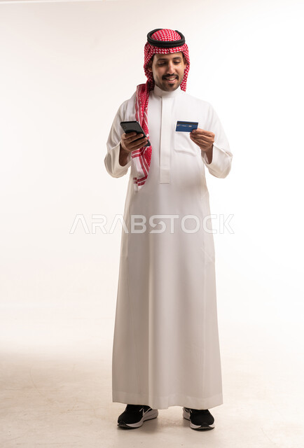 رجل سعودي بالثوب يحمل بطاقة ائتمانية وهاتف ذكي