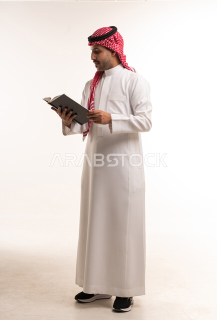 رجل سعودي بالزي التقليدي يقرأ كتاباً في الاستوديو