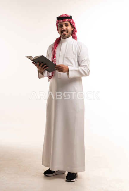 رجل سعودي بالزي التقليدي يحمل كتاباً أمام خلفية بيضاء