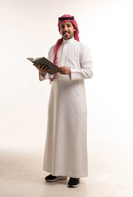 رجل سعودي بالزي التقليدي يحمل كتاباً أمام خلفية بيضاء