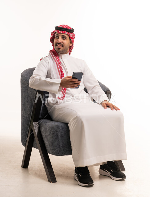 رجل سعودي يحمل هاتف ذكي جالس على كرسي في الاستوديو