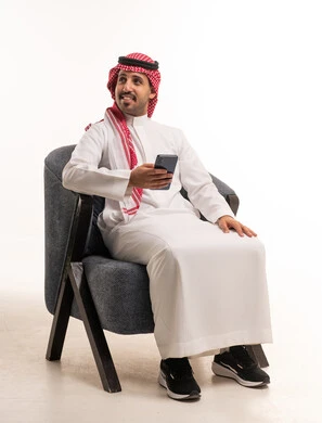 رجل سعودي يحمل هاتف ذكي جالس على كرسي في الاستوديو