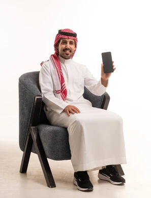 رجل سعودي بالزي التقليدي يحمل هاتفاً ذكياً