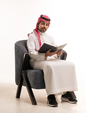Saudi Man in Traditional Thobe Reading Book on Armchair