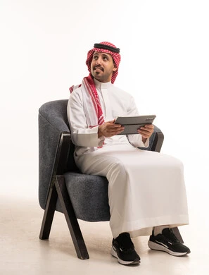 رجل سعودي بالزي التقليدي يستخدم جهاز لوحي على كرسي