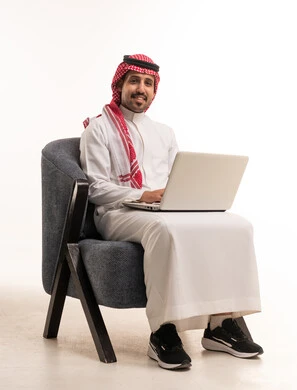 رجل سعودي بالزي التقليدي يستخدم حاسوب محمول على خلفية بيضاء