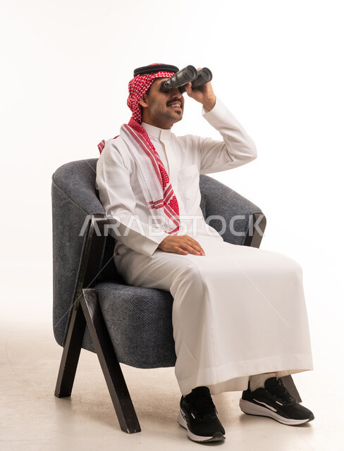 رجل سعودي بالثوب التقليدي يستخدم المنظار في الاستوديو