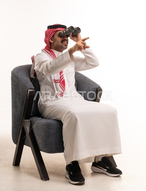 Saudi Man in Traditional Thobe Using Binoculars Indoors