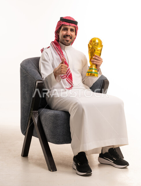 رجل سعودي بالثوب يحمل كأساً ذهبياً أمام خلفية بيضاء