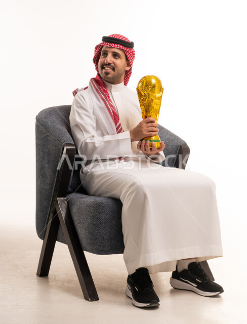رجل سعودي بالزي التقليدي يحمل مجسم كأس العالم الذهبي