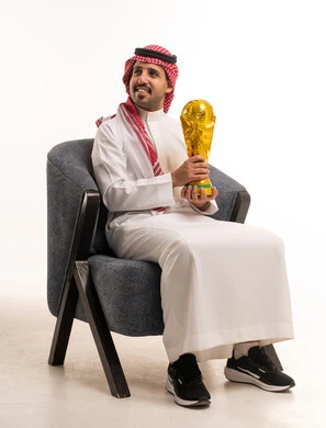 رجل سعودي بالزي التقليدي يحمل مجسم كأس العالم الذهبي