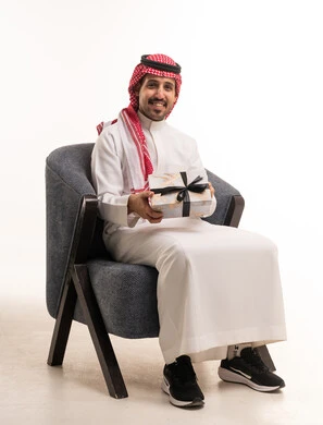 رجل سعودي يحمل صندوق هدايا على كرسي خلفية بيضاء