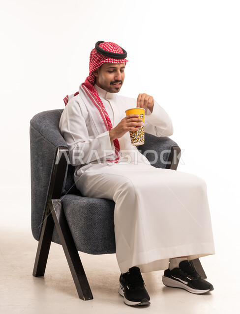 رجل سعودي بالزي التقليدي يأكل الفشار