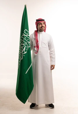 رجل سعودي بالزي التقليدي يمسك علم المملكة العربية السعودية