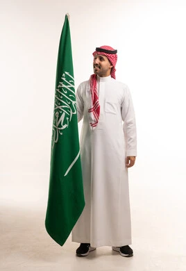 رجل سعودي يحمل العلم الوطني على خلفية بيضاء