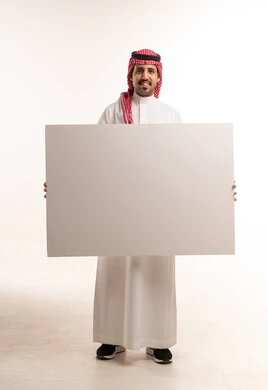 رجل سعودي يمسك لوحة بيضاء فارغة في استوديو