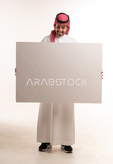 رجل سعودي بالزي التقليدي يمسك لوحة بيضاء فارغة