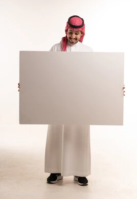 رجل سعودي بالزي التقليدي يمسك لوحة بيضاء فارغة