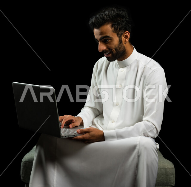 رجل عربي سعودي خليجي يرتدي الزي السعودي، إستخدام جهاز اللابتوب لإنجاز المهام، التسوق الإلكتروني، تطور التكنولوجيا وإستخدام الأجهزة التقنية الحديثة، إجتماع عمل، إدارة الأعمال عن بعد، تصفح الانترنت, إجراء مكالمات فيديو عبر جهاز الحاسوب, خلفيه سوداء